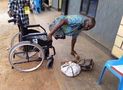 A Rwandan man with both legs amputated uses his new wheelchair from the Wheels for the World initiative to transfer from the ground beside his bags.
