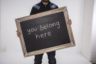 A person holds a large chalkboard sign with the handwritten message you belong here, celebrating each step of the ABC Journey.