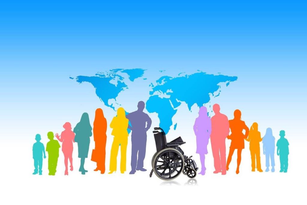 A group of colorful human and wheelchair silhouettes stands before a blue world map on a gradient background. (source: inclusion-3976157_1280_pixabay)