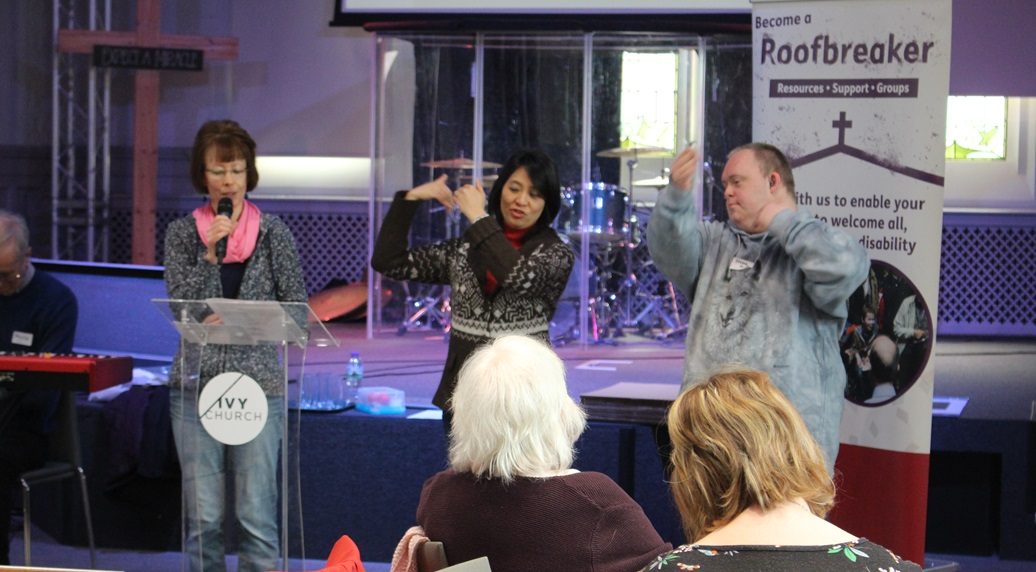 Three people stand on stage at Ivy Church, addressing an audience while communicating through speech and sign language.