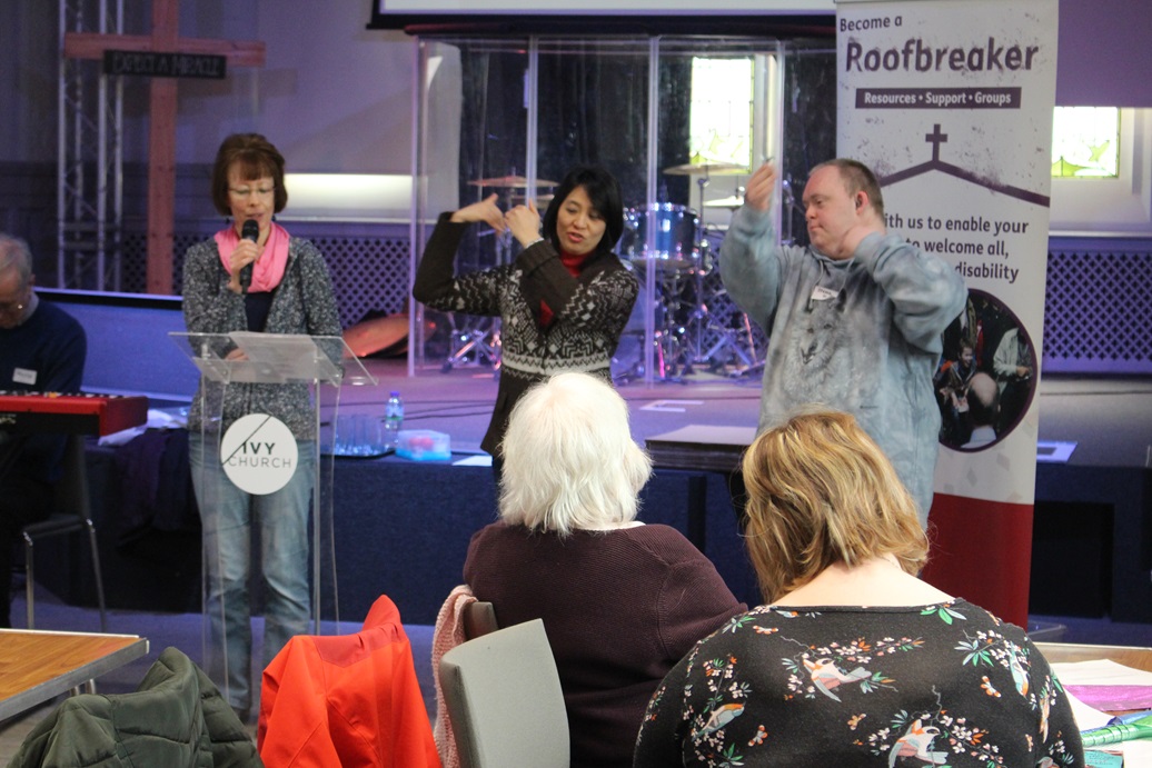 Three people stand on stage at Ivy Church, addressing an audience while communicating through speech and sign language.